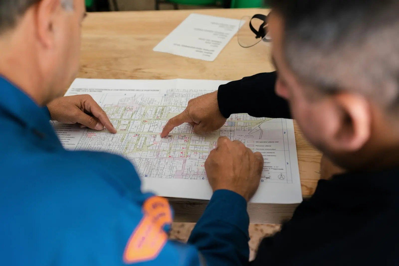 Deux employés en uniforme suivent du doigt un plan imprimé sur une table de travail.