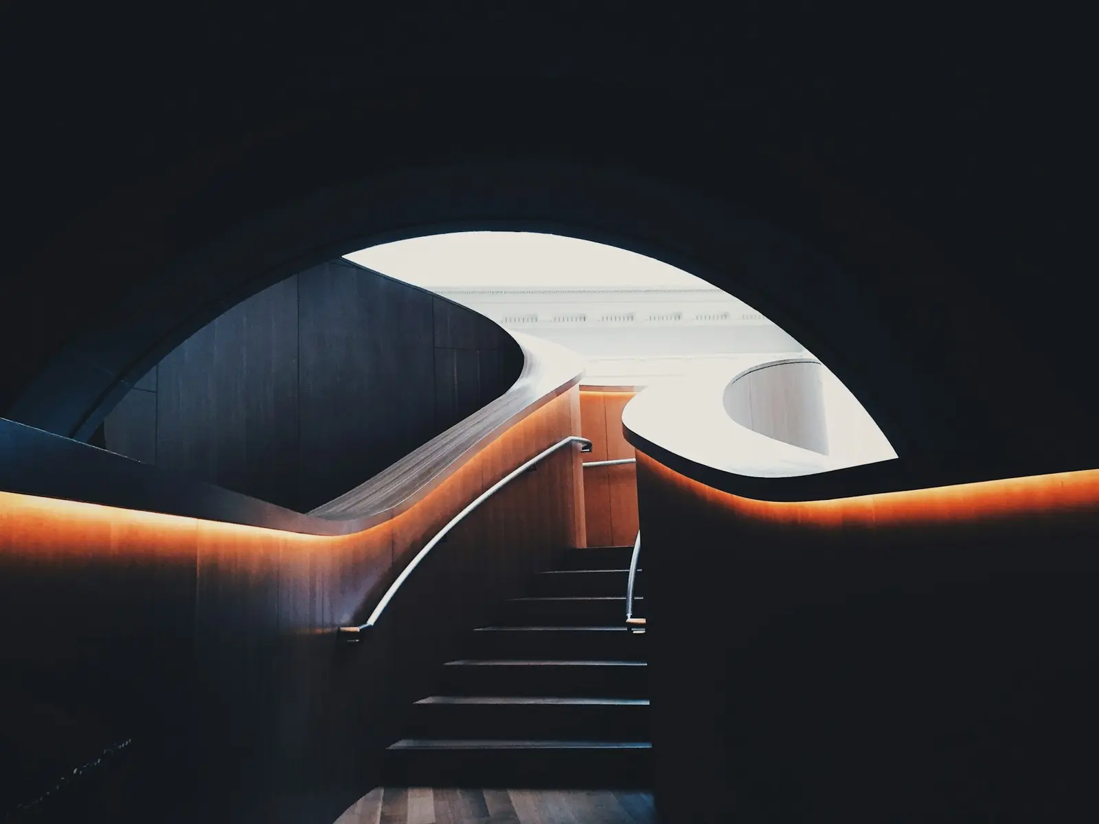 A dark staircase lit by a thin orange line, inside sculpted architecture