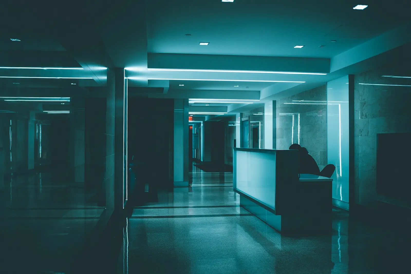 A turquoise hospital corridor and its reception desk, in half light