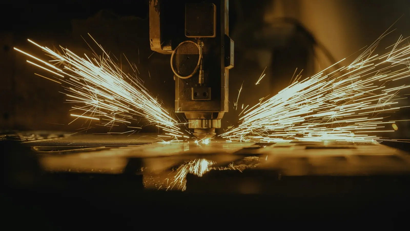 A laser cutter throwing sprays of sparks across a metal plate