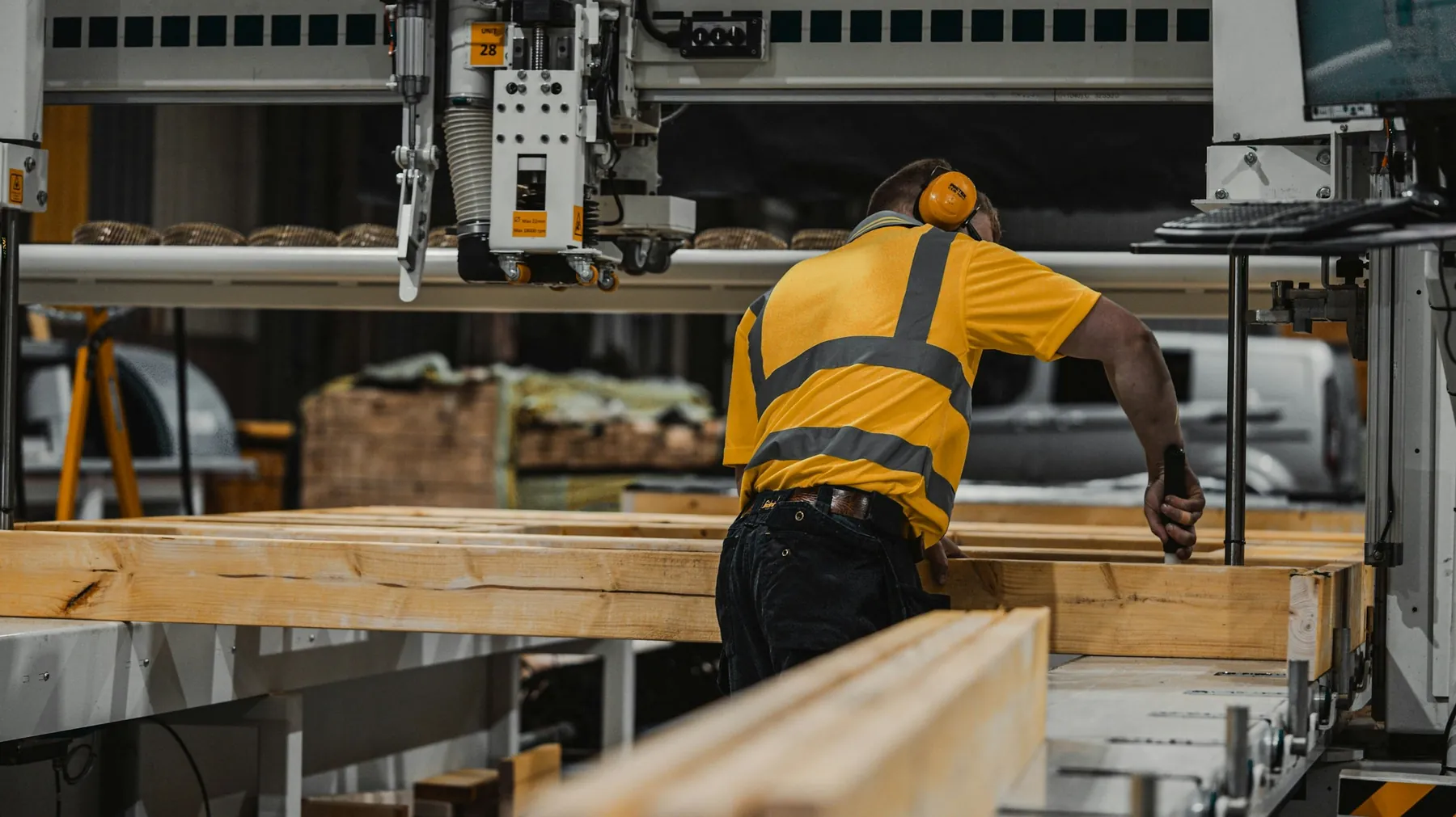 A worker in a high-visibility shirt sets up a CNC saw in a lumber plant.